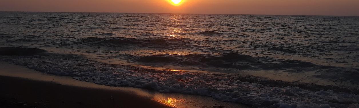 a sun begins to descend to the horizon on a beach at Lake Erie